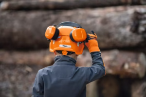 Dziecko stojące tyłem w kompletnym stroju, regulujące zabawkowy hełm STIHL dla dzieci.